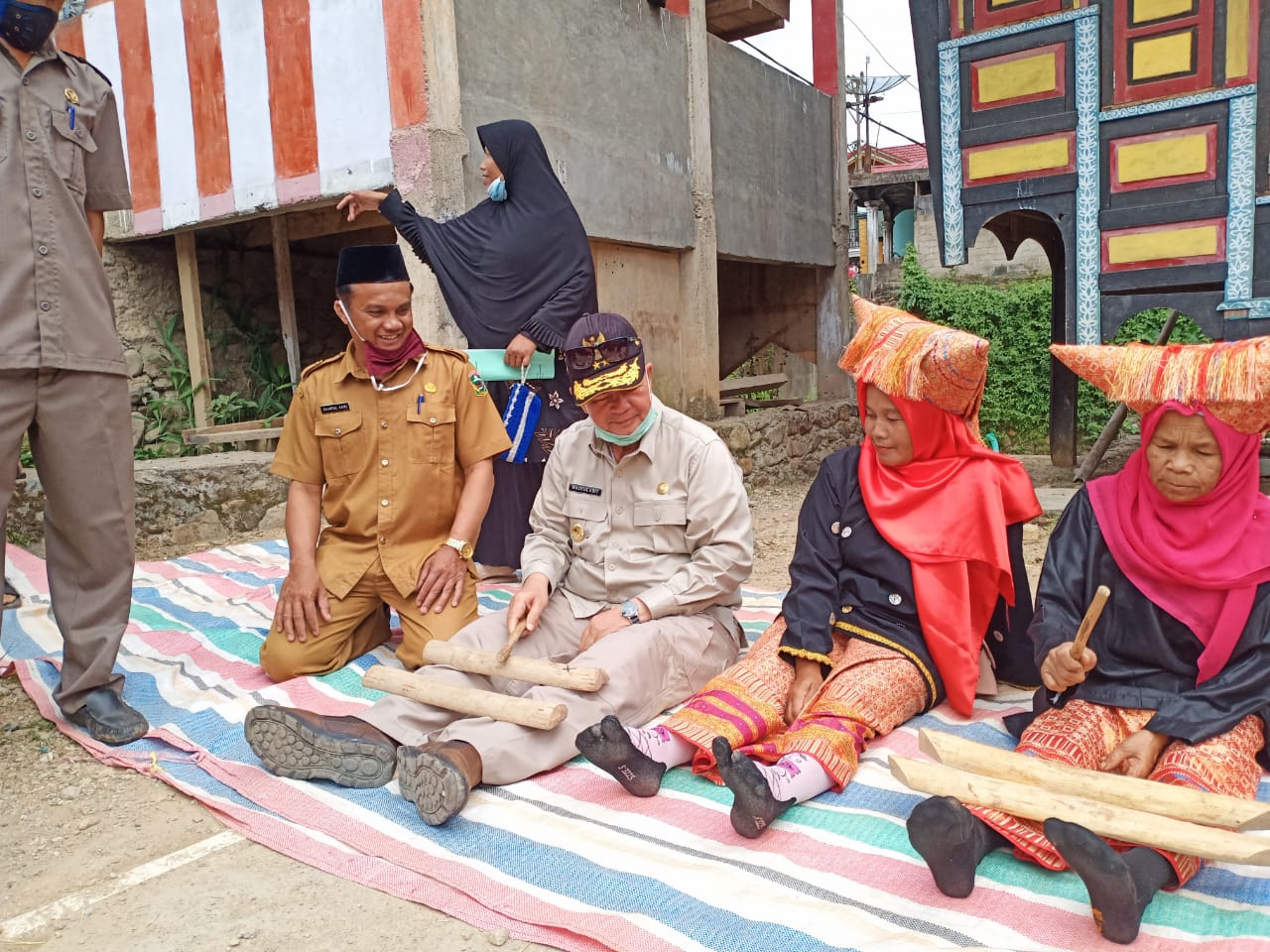 Wakil Gubernur Sumbar, Nasrul Abit, ikut duduk berselonjor belajar memainkan musik tradisional yang menggunakan dua potong kayu, di nagari Batu Bajanjang. Foto Biro Humas Setdaprov Sumbar. 