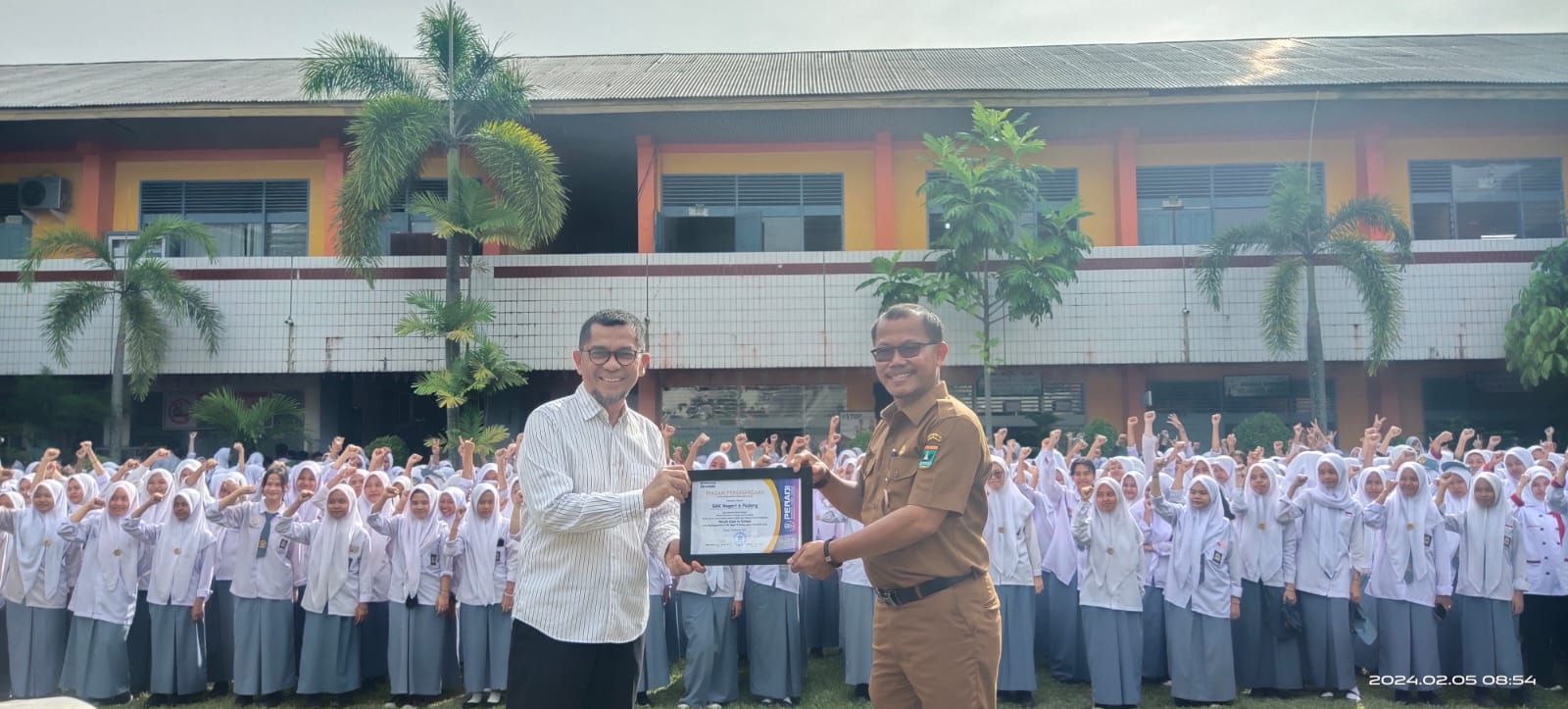 Ketua DPC Peradi Padang Miko Kamal, Ph.D, menyerahkan penghargaan kepada kepala sekolah Deta Mahendra, SP.d., MM., di lapangan upacara SMK Negeri 6 Padang, Senin (5/2/2024). Foto ist.