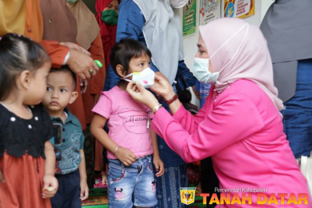 Ketua TP PKK Ny Retri Zuldafri memasangkan masker pada seorang balita.