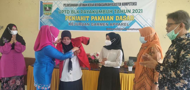 Kepala Dinas Tenaga Kerja dan Perindustrian Kota Payakumbuh Yunida Fatwa memasangkan baju peserta pelatihan menjahit pakaian dasar Kejuruan Garmen Apparel di UPTD BLK Payakumbuh